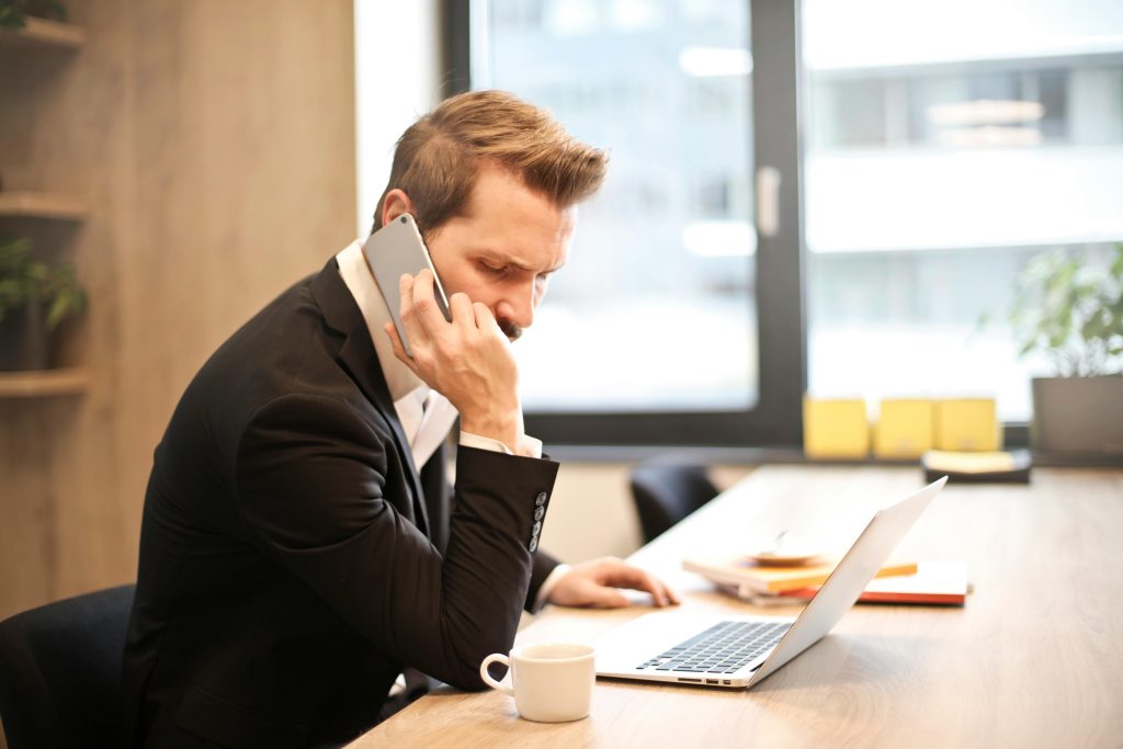 Nagrania Rozmów A businessman in a suit making a phone call while working on a laptop in a modern office setting.